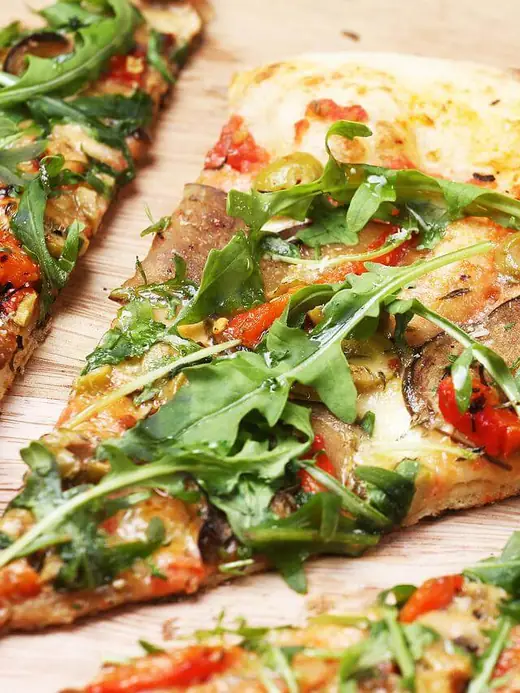 Pizzastück mit Rucola, Oliven und gegrilltem Gemüse